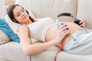 Beautiful pregnant woman holding headphones on her belly while lying on sofa